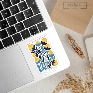 Könnte beinhalten: Ein weißer Aufkleber mit einem floralen Design aus gelben und blauen Blumen und dem Text "HE RESTORES MY SOUL PSALM 23:3". Der Aufkleber befindet sich auf einem Laptop.