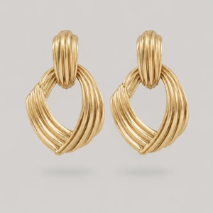 May include: A pair of gold-toned earrings featuring a vertical ribbed top section connected to a larger, open, oval-shaped bottom piece with a series of diagonal, raised, ribbed lines that create a textured, layered appearance throughout the design.
