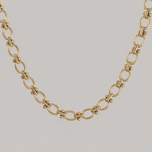 Peut inclure: Un collier à chaîne en métal doré composé d'un motif répétitif de maillons ovales allongés. Chaque maillon ovale est relié par un petit segment de barre horizontale, orné de deux minuscules perles sphériques de chaque côté du point de jonction.