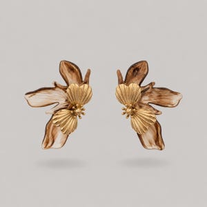 May include: A pair of earrings featuring a floral design with gold-toned, ribbed petals layered over larger, smooth, brown and white marbled petals. The earrings have a distinct organic shape with multiple overlapping leaf-like elements.