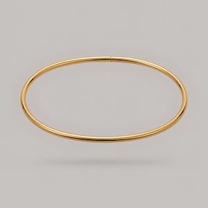 May include: A thin, circular gold bangle bracelet with a smooth, polished finish. The jewelry piece features a simple, continuous hoop design with a subtle seam visible at the top, showcasing a reflective metallic surface and a uniform, rounded profile.