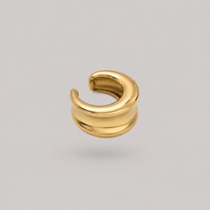 Pode incluir: Um ear cuff de tom dourado com um design em forma de C, liso, polido e arredondado. A peça de joalharia apresenta uma banda espessa e contínua com uma superfície metálica refletora e uma abertura larga, exibindo uma estrutura sólida.