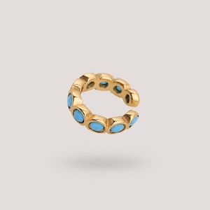 May include: A gold-toned ear cuff featuring a series of small, round, bright blue turquoise-colored stones set in a continuous circular band. The metal has a polished finish, and the design is open at one side to allow for placement on the ear.