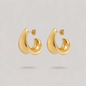 May include: A pair of gold-toned hoop earrings featuring a smooth, polished, and curved teardrop silhouette. Each earring has a post-back closure mechanism and a reflective, high-shine metallic finish that catches the light evenly across the surface.