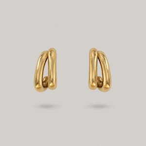 May include: A pair of gold-toned earrings, each featuring two smooth, polished, interlocking curved metal loops that create an open, elongated oval shape. The earrings have a reflective, high-shine finish and a simple, continuous design.