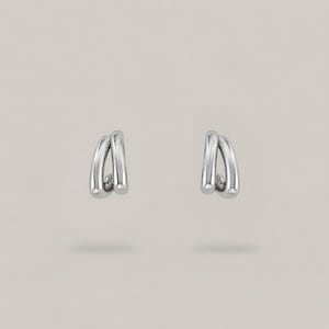 May include: A pair of silver-toned hoop earrings, each featuring a double-loop design with a smooth, polished metallic finish. The earrings have a curved, open structure that creates a layered appearance, reflecting light on their rounded surfaces.