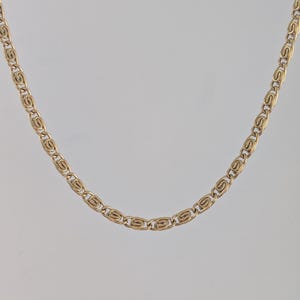 May include: A gold-colored chain necklace with a repeating oval link design. The necklace is displayed against a neutral background, highlighting its intricate pattern and warm metallic tone. The chain is a jewelry item.