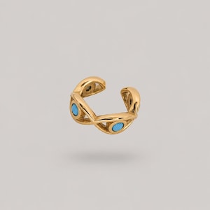 May include: A gold-toned ear cuff featuring an open, twisted band design. The metal structure is accented with three small, round, bright turquoise blue stones embedded at intervals along the curved, polished surface of the jewellery piece.