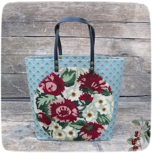 Peut inclure: Un sac fourre-tout bleu clair avec un motif floral. Le sac présente un motif brodé circulaire de fleurs rouges et blanches avec des feuilles vertes. Il a des poignées en cuir noir et des rivets dorés.