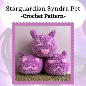 Könnte beinhalten: Drei lila gehäkelte Plüschtiere in Katzenform mit rosafarbenen Gesichtszügen. Die Spielzeuge sind übereinander gestapelt. Das Bild ist mit "Stargurdian Syndra Pet -Crochet Pattern- " betitelt.