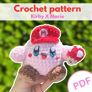 Könnte beinhalten: Eine Häkelanleitung als PDF mit dem Titel Crochet pattern Kirby X Mario, die eine hellrosa Plüschfigur mit einer roten Mütze mit weißem M-Emblem, braunen Füßen, blauen Augen und einem kleinen rot-weiß gepunkteten Pilz in der Hand zeigt.