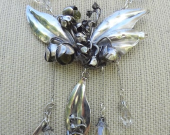 May include: A silver necklace with a floral pendant featuring leaves and flowers. The pendant is attached to a chain with crystal beads.