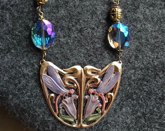 May include: A gold necklace with a large pendant featuring a stylised floral design with dragonfly wings. The pendant is decorated with purple, pink and green enamel. The necklace is made with pink and purple beads.