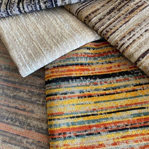 Könnte beinhalten: Eine Auswahl an strukturierten Stoffmustern mit Streifenmustern. Die Stoffe zeigen eine Reihe von Farben, darunter Beige, Braun, Orange, Gelb, Blau und Schwarz. Diese Textilien sind wahrscheinlich für Polster- oder Heimdekorationszwecke bestimmt.