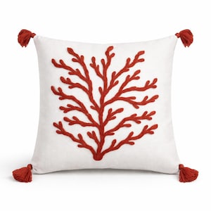 Pode incluir: Almofada decorativa quadrada branca com um design bordado vermelho semelhante a coral. A almofada tem quatro borlas vermelhas, uma em cada canto. O design é uma representação estilizada de coral ou uma árvore.