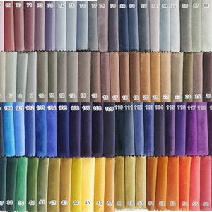 Op de afbeelding: Een kleurstalen display met een breed scala aan stofstalen in verschillende tinten. De stalen zijn gerangschikt in rijen en kolommen en tonen een spectrum aan kleuren, van neutrale tinten tot levendige tinten. Elke staal is genummerd.