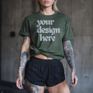 May include: A woman wearing a green t-shirt with the text "your design here" in a glitched font. She is also wearing black athletic shorts.