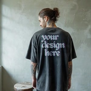 Könnte beinhalten: Dunkelgraues übergroßes T-Shirt mit dem Text "your design here" in 3D-Effekt. Das Shirt hat einen Vintage-Look. Das Model ist von hinten zu sehen.