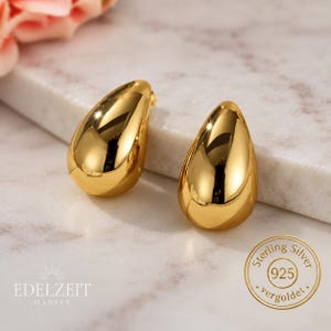Könnte beinhalten: Ein Paar goldfarbene tropfenförmige Ohrringe mit einer glatten, reflektierenden Oberfläche. Die Ohrringe haben ein poliertes Finish und ein abgerundetes, bauchiges Design. Ein kreisförmiger Stempel zeigt Sterling Silver 925 vergoldet.