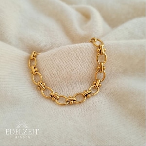 Könnte beinhalten: Ein goldenes Kettenarmband mit einem zarten, verlinkten Design. Jeder Link hat einen kleinen, runden Akzent.