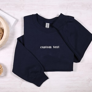 May include: A navy blue sweatshirt with the text "custom text" embroidered on the front.