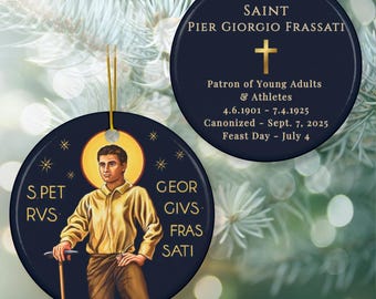 May include: Navy blue round Christmas ornament depicting Saint Pier Giorgio Frassati. The ornament has gold text and a gold cross. Text includes the saint's name, dates, and title as patron of young adults and athletes. A festive holiday decoration.