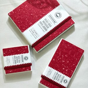 May include: Three watercolor paper journals with red speckled covers and white labels. The labels read "DECKLE EDGED WATERCOLOR PAPER JOURNAL" and include the brand name "POTENTATE". Each journal is bound with a red elastic band. The journals are 19cm x 19cm.