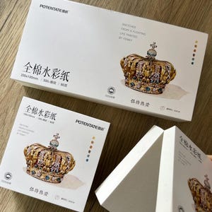 K&ouml;nnte beinhalten: Wei&szlig;e Aquarellpapierboxen mit goldenen Kronenillustrationen. Die Boxen tragen chinesischen und englischen Text, darunter "Sketches From a Floating Life Painted by Fenny". Die Papierma&szlig;e sind 200x100mm und 100x100mm.