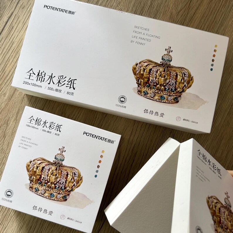 K&ouml;nnte beinhalten: Wei&szlig;e Aquarellpapierboxen mit goldenen Kronenillustrationen. Die Boxen tragen chinesischen und englischen Text, darunter "Sketches From a Floating Life Painted by Fenny". Die Papierma&szlig;e sind 200x100mm und 100x100mm.