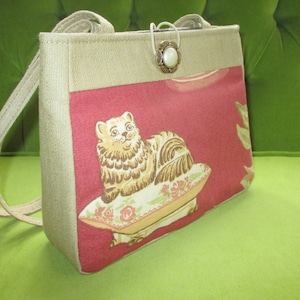 Peut inclure: Un sac fourre-tout en tissu beige et rouge avec un motif de chat et une fermeture à bouton décorative. Le chat est assis sur un coussin à motifs floraux.