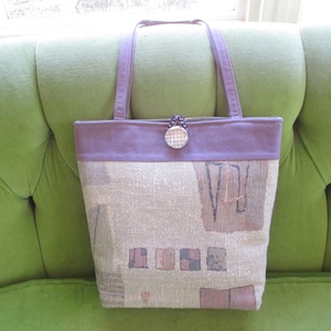 Pode incluir: Uma bolsa tote roxa e bege com um design de tapeçaria e um fecho de botão prateado.