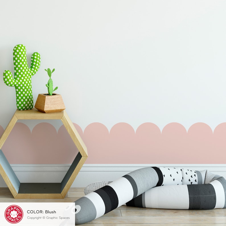 May include: A pink scalloped border wall decal with a white background. The decal is shown in a room with a wooden shelf and a cactus and a small plant on the shelf. There is a black and white striped pillow on the floor. COLOR: Blush. Copyright &copy; Graphic Spaces