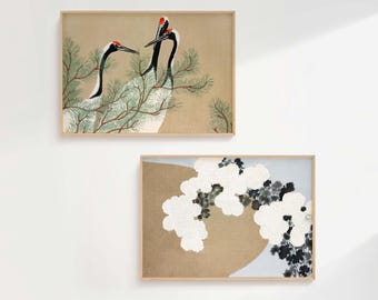 May include: Two framed art prints. The top print features three cranes with red crowns and black and white feathers, perched on a pine branch. The bottom print shows white flowers and dark foliage against a tan and blue background.