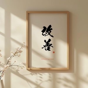 Op de afbeelding: Een ingelijst afdruk met zwarte kalligrafie in een wit frame. De kalligrafie luidt "改善", wat vertaalt naar "Continue verbetering".