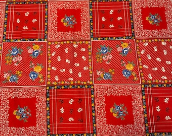 May include: Red fabric with a patchwork design. The fabric features squares with floral patterns, polka dots, and plaid accents. The floral patterns include blue, yellow, and pink flowers. The fabric is likely used for quilting or crafting.
