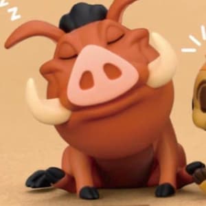 May include: A figurine of Pumbaa from The Lion King, in a seated position with closed eyes, appearing to be sleeping. The figure is primarily brown with a pink snout, white tusks, and black hair. The base of the figurine has Japanese text.
