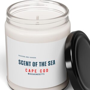Op de afbeelding: Een witte kaars in een heldere glazen pot met een zwarte deksel. Het etiket luidt "Scent of the Sea, Cape Cod, Massachusetts". De kaars is gelabeld "Seaside Dry Goods".