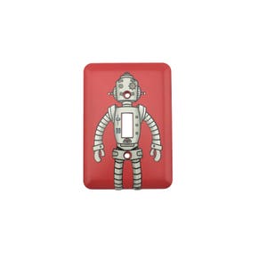 May include: A red light switch cover featuring a robot design. The robot is silver and has a round head with a single eye. The robot has two arms and two legs.