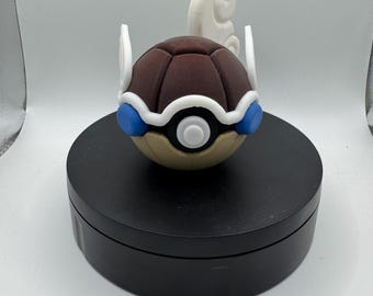 May include: A brown and tan decorative ball with white and blue accents, resembling a stylized turtle shell. The ball has a white swirl design on top and is set on a black circular base. The overall design is reminiscent of a popular animated series.