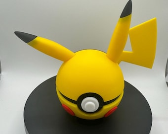 May include: A yellow Pikachu-themed Poké Ball with black-tipped ears and tail, red accents, and a white button. The ball is set on a black circular base, showcasing a popular character from the Pokémon franchise.