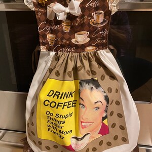 Könnte beinhalten: Ein weißes Geschirrtuch mit brauner Spitzenborte und einem braunen und weißen Kaffeemuster. Der Druck zeigt Kaffeetassen, Kaffeebohnen und den Text "Drink Coffee Do Stupid Things Faster with More Energy".