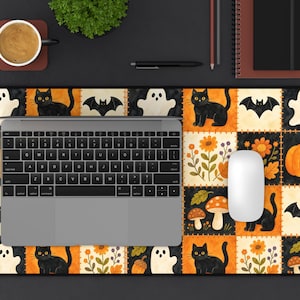 May include: A rectangular desk mat featuring a patchwork pattern of Halloween-themed illustrations including black cats, white ghosts, orange pumpkins, bats, mushrooms, and autumn flowers in shades of orange, yellow, and black on a dark background.