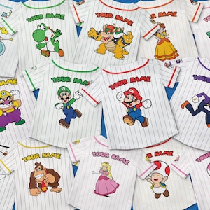 May include: White baseball-style shirts with pinstripes and colorful cartoon character graphics. Each shirt has "YOUR NAME" printed above the character. Characters include Mario, Luigi, Yoshi, and Princess Peach.