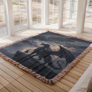 May include: A dark blue throw blanket featuring a dragon and rider silhouette against a stormy sky. The blanket has a fringed edge and includes the text: "A dragon without its rider is a tragedy. A rider without their dragon is dead."
