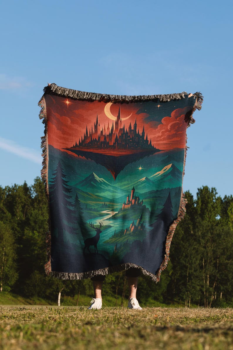 Peut inclure: Une couverture en tapisserie repr&eacute;sentant un paysage fantastique avec un ch&acirc;teau, des montagnes et un cerf. La couverture a une bordure &agrave; franges et une palette de couleurs de bleus profonds, de verts et de rouges. Le ciel est un d&eacute;grad&eacute; de rouge et de bleu.