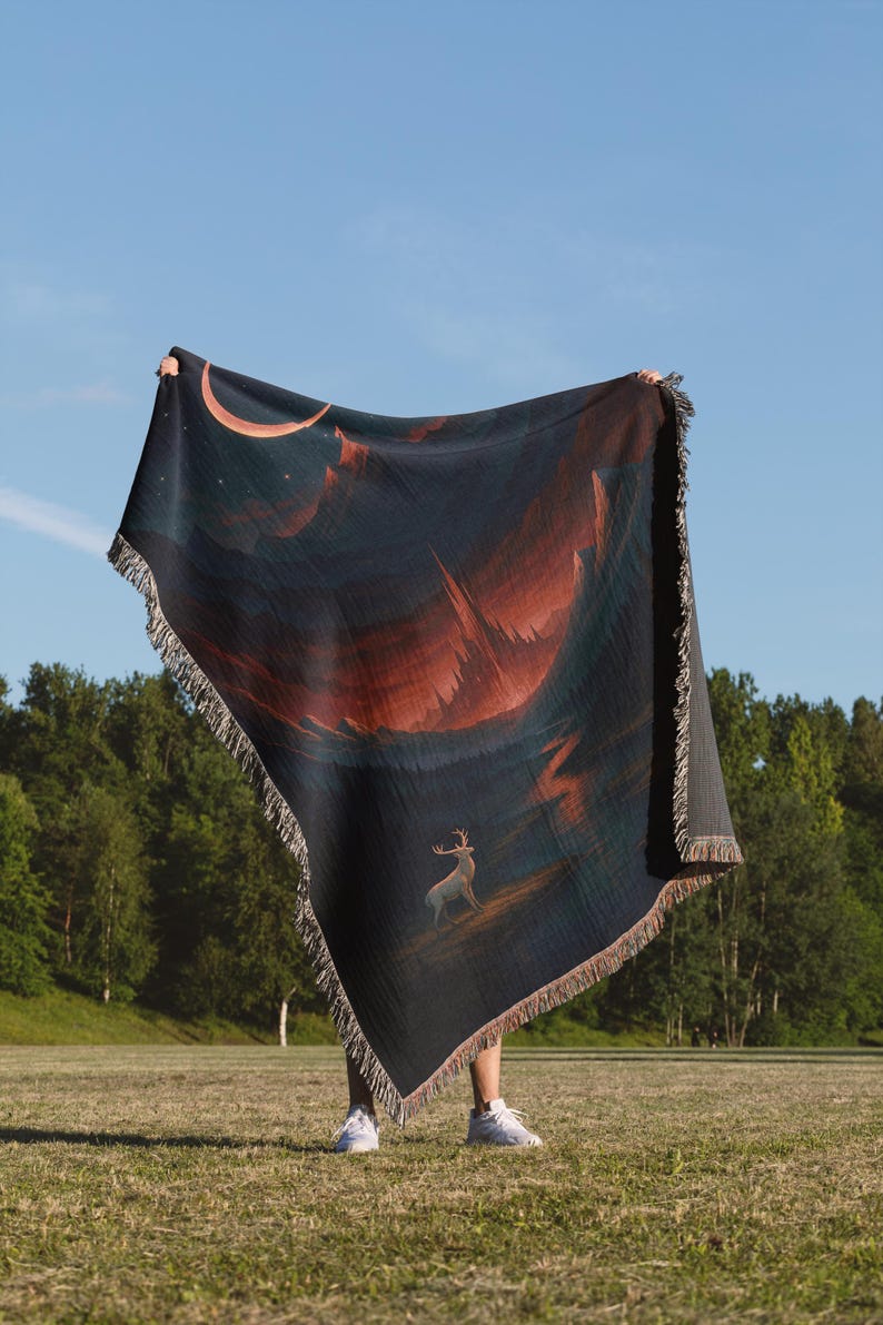 Peut inclure: Une couverture bleu fonc&eacute; avec un motif de paysage repr&eacute;sentant un cerf, un croissant de lune et une cha&icirc;ne de montagnes dans des tons orange et rouge. La couverture a une bordure &agrave; franges.