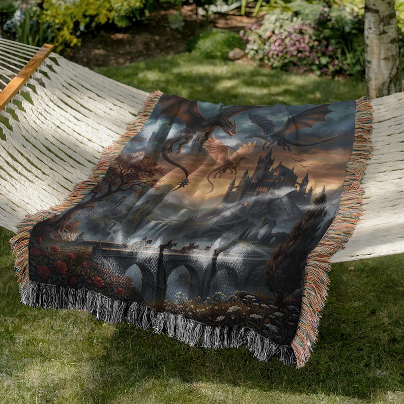 Pu&ograve; includere: Una coperta tessuta con un paesaggio fantasy con draghi, un castello e un ponte. La coperta presenta un'illustrazione dettagliata nei toni del blu, dell'arancione e del marrone, con un bordo a frange. La coperta &egrave; drappeggiata su un'amaca.