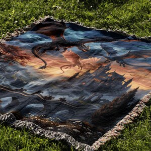 Pu&ograve; includere: Una coperta rettangolare con una scena fantasy. L'opera d'arte raffigura draghi, un castello e un ponte. I draghi volano contro un cielo al tramonto, con un castello e un ponte in primo piano. La coperta ha un bordo con frange.
