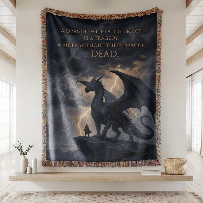 May include: Woven tapestry featuring a dramatic dragon illustration with a rider on a cliff against a stormy sky. The text reads: "A DRAGON WITHOUT ITS RIDER IS A TRAGEDY. A RIDER WITHOUT THEIR DRAGON IS DEAD."