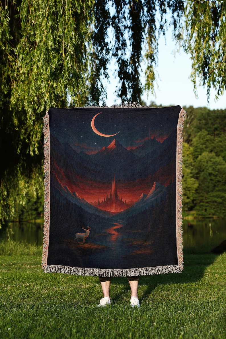 Peut inclure: Plaid tiss&eacute; repr&eacute;sentant un paysage fantastique avec un croissant de lune, des montagnes et un cerf. La palette de couleurs comprend des bleus fonc&eacute;s, des rouges et des oranges. La couverture a une bordure &agrave; franges.